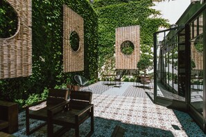 An outdoor patio with wicker furniture, a patterned floor, and a glass enclosure with a view of the greenery. - Hotel Praktik Vinoteca (Barcelona)