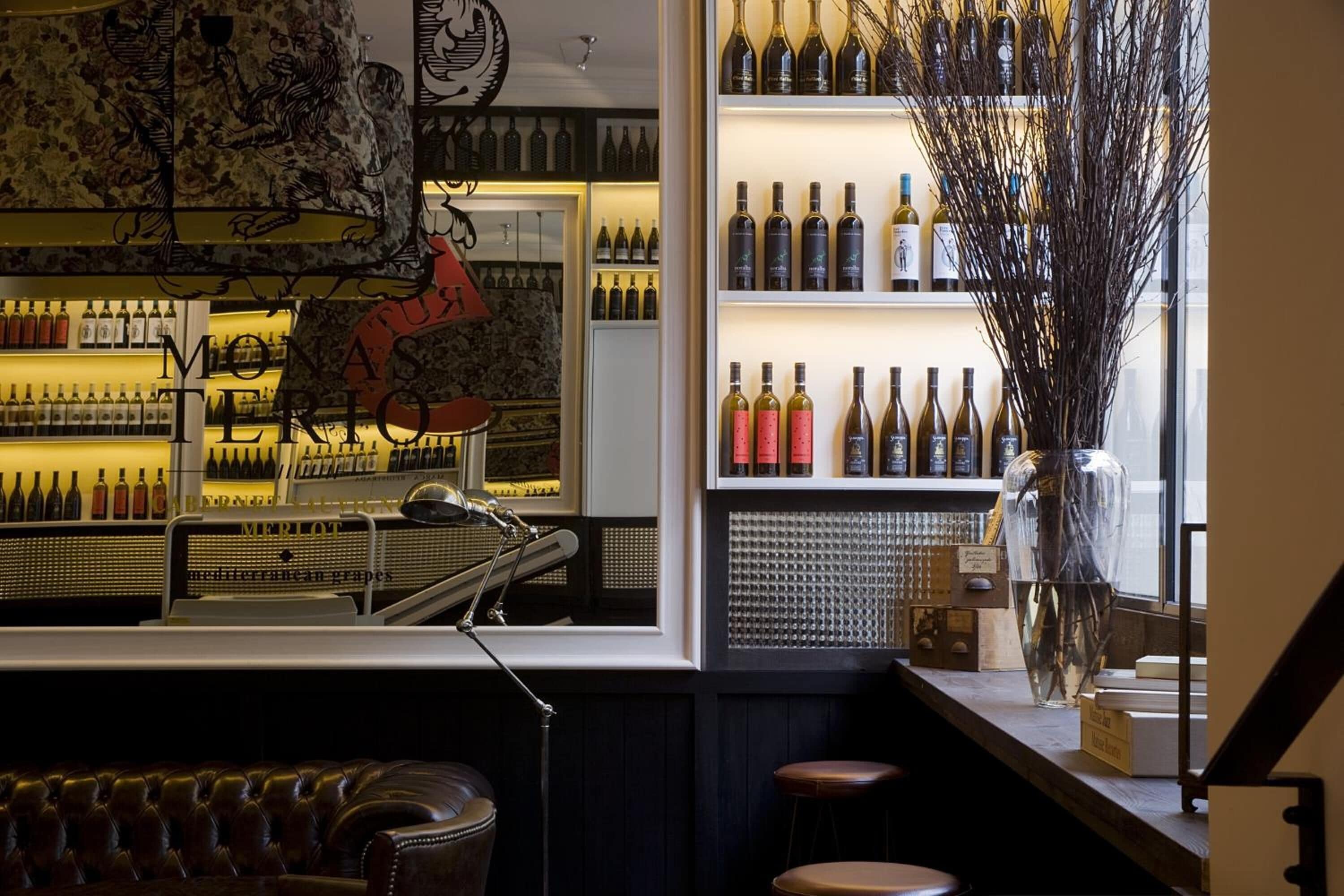 A bar area with shelves of wine bottles, a leather couch, and a decorative vase.