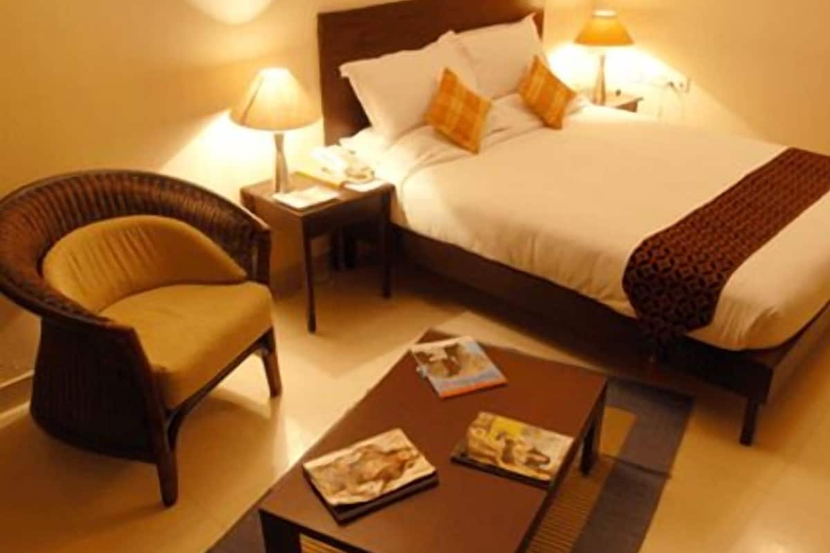 A hotel room with a bed, a chair, a nightstand, and a table with magazines.
