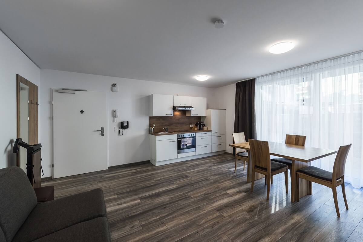 Een moderne keuken met witte kasten, een inbouwoven en een eethoek met een houten tafel en stoelen.