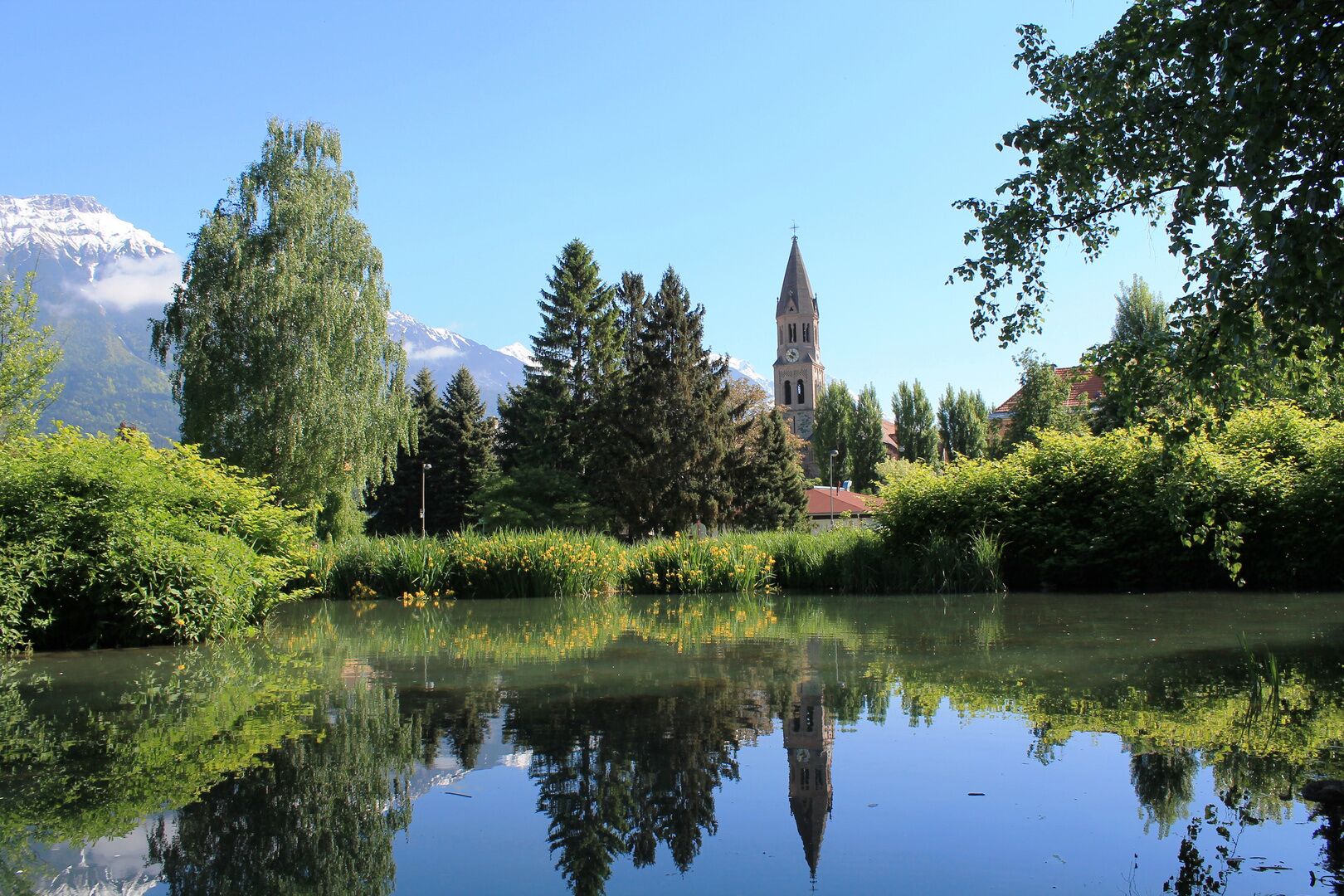 Een vredig uitzicht op een meer met een kerktoren, weelderige begroeiing en een berg op de achtergrond.