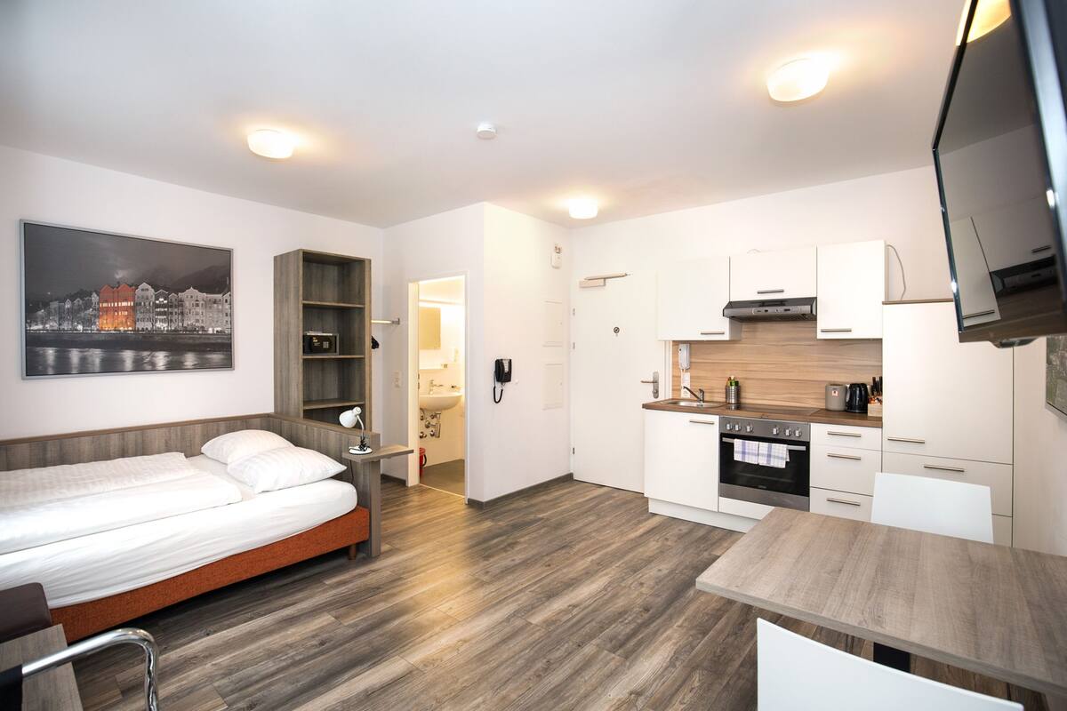 Een moderne hotelkamer met een bed, een kleine kitchenette, een eethoek en een badkamer.