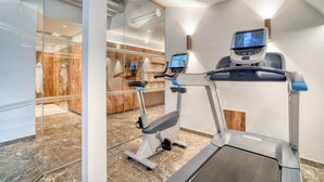 Un gimnasio moderno con cinta de correr, elíptica y pantalla de televisión en la pared.