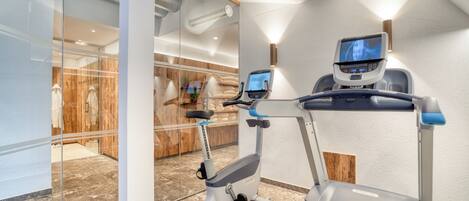 A modern gym with a treadmill, an elliptical, and a wall-mounted TV screen.