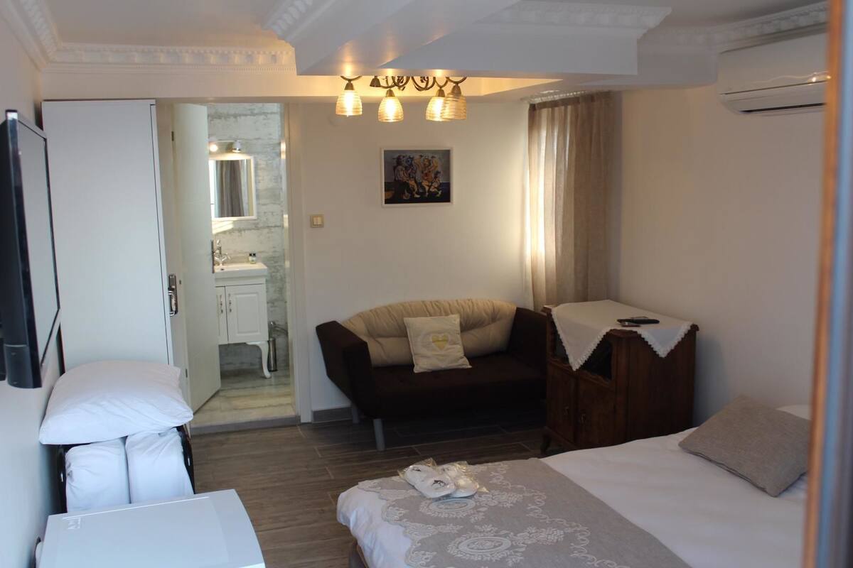 A hotel room with a bed, a sofa, a desk, a chair, a small table, and a bathroom visible through an open door.