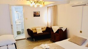 A hotel room with a bed, a sofa, a wooden cabinet, and a small kitchenette in the background. - Silenos Boutique Hotel (Seferihisar)