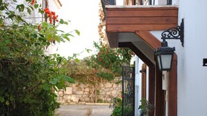 A cobblestone street with a stone wall and greenery on one side, and a building with a wooden balcony and a black wrought iron gate on the other. - Silenos Boutique Hotel (Seferihisar)