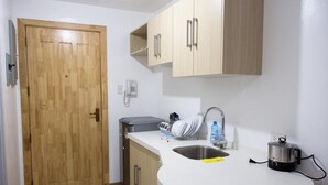 Une cuisine avec une porte en bois, un évier, des placards, un égouttoir et une bouilloire.