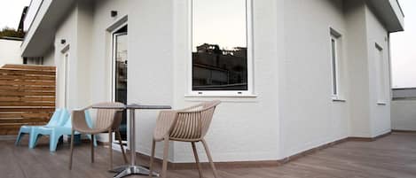A modern building with a flat roof, a balcony with a table and chairs, and a large window.