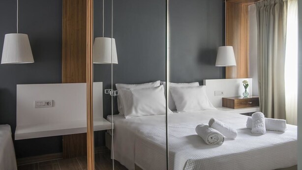 A modern hotel room with a large bed, bedside tables, a nightstand, and a mirror. - AD Luxury Rooms & Suites (Athens)