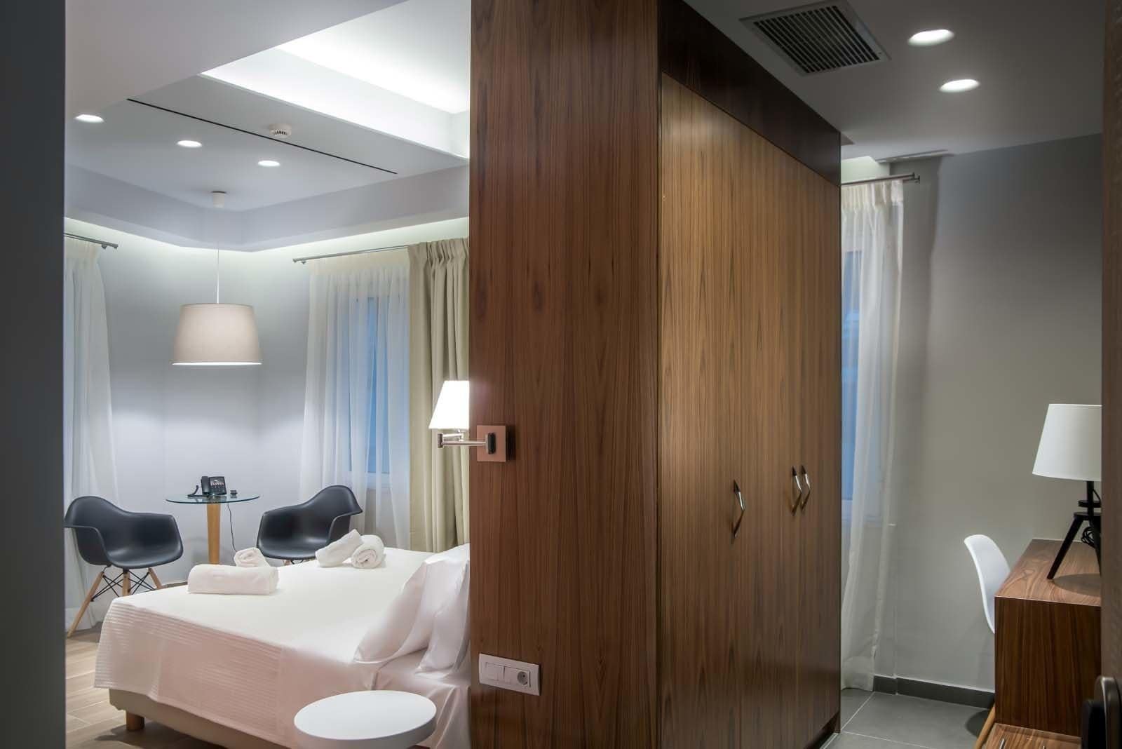 A hotel room with a bed, a desk, two chairs, a wardrobe, and a bathroom.