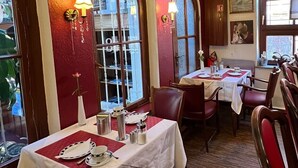 Un comedor con mesas dispuestas para dos, ventanas arqueadas amplias y un candelabro.