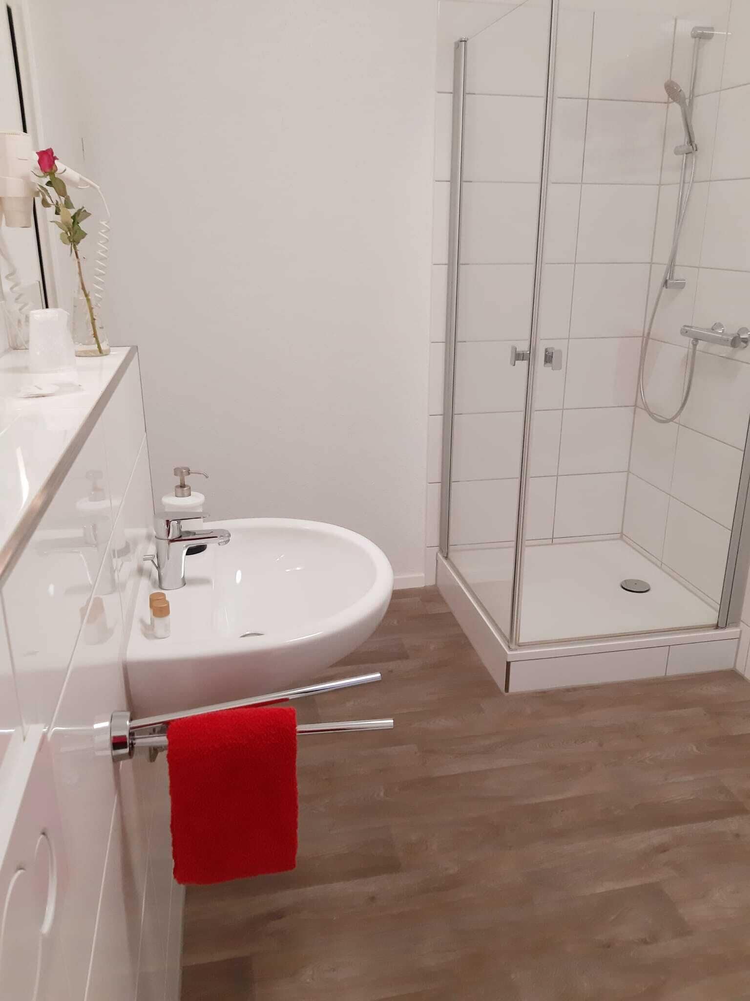 Un baño moderno con lavamanos blanco, cabina de ducha de vidrio y suelo de madera.