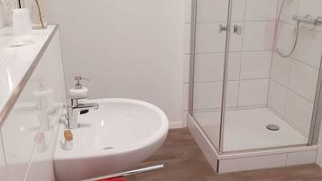 Un baño moderno con lavamanos blanco, cabina de ducha de vidrio y suelo de madera.