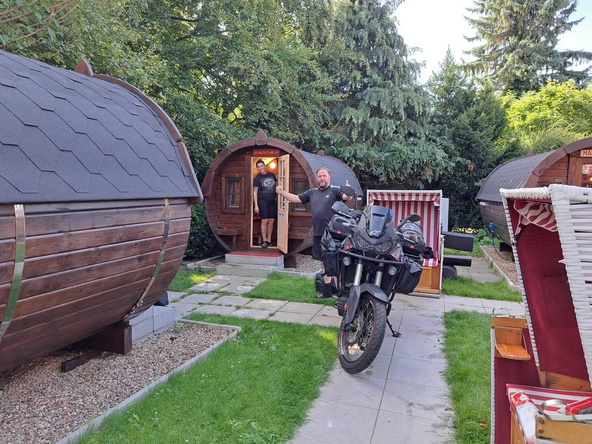 A motorcycle parked in front of a wooden structure with a door labeled "Kleines Haus".