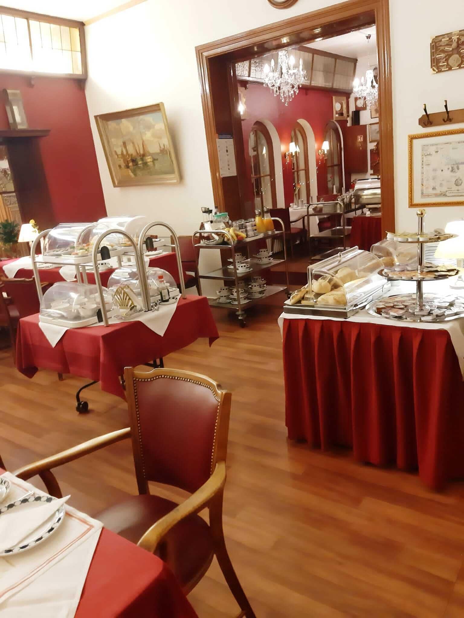 Un comedor con varias mesas cubiertas con manteles rojos, equipado con estaciones de buffet y diferentes tipos de comida.
