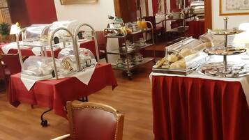 Un comedor con varias mesas cubiertas con manteles rojos, equipado con estaciones de buffet y diferentes tipos de comida.