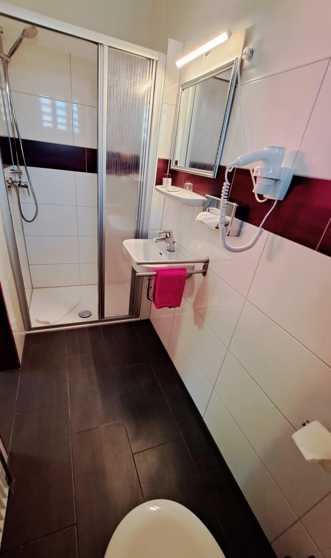 A bathroom with a glass shower enclosure, a white sink with a mirror above it, and a hairdryer on the wall.