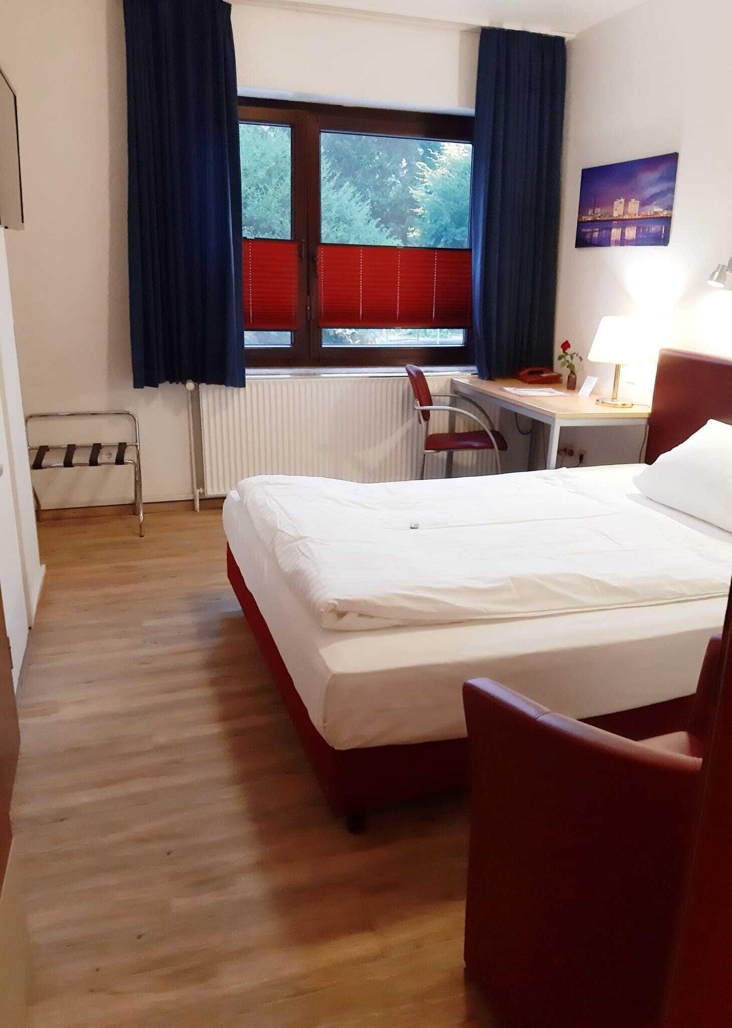 Ein Hotelzimmer mit Bett, Schreibtisch, Stuhl, Heizkörper und einem fensterbepflanzten Fenster.