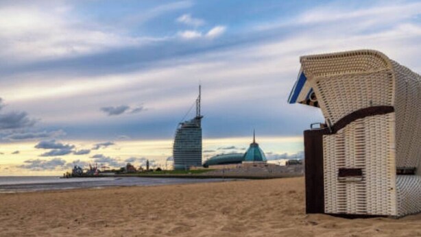 Una playa con una silla de mimbre y un edificio moderno al fondo.