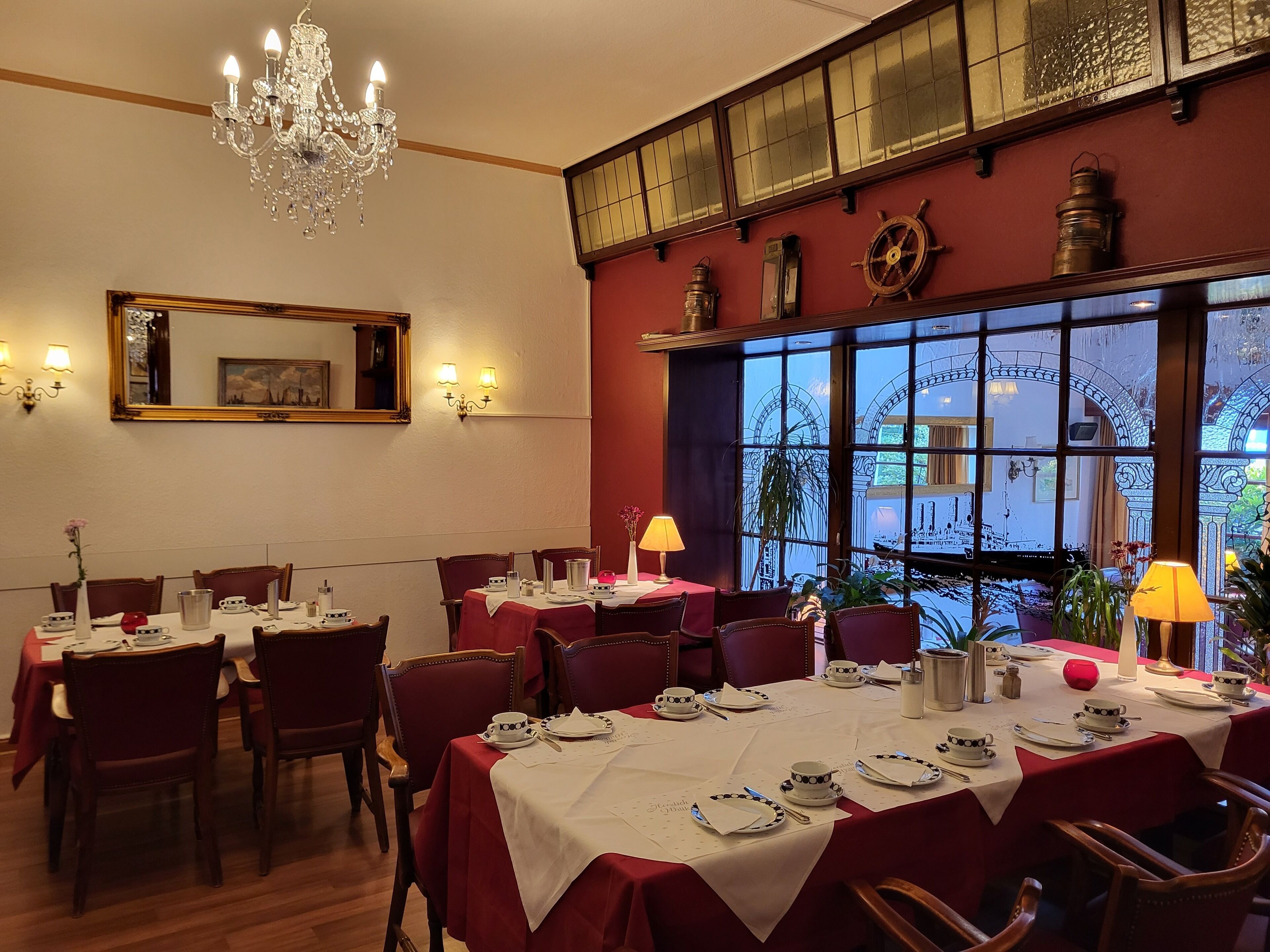 A dining area with tables set for service, a chandelier, and a large window with decorative ironwork.