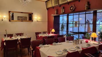 A dining area with tables set for service, a chandelier, and a large window with decorative ironwork.
