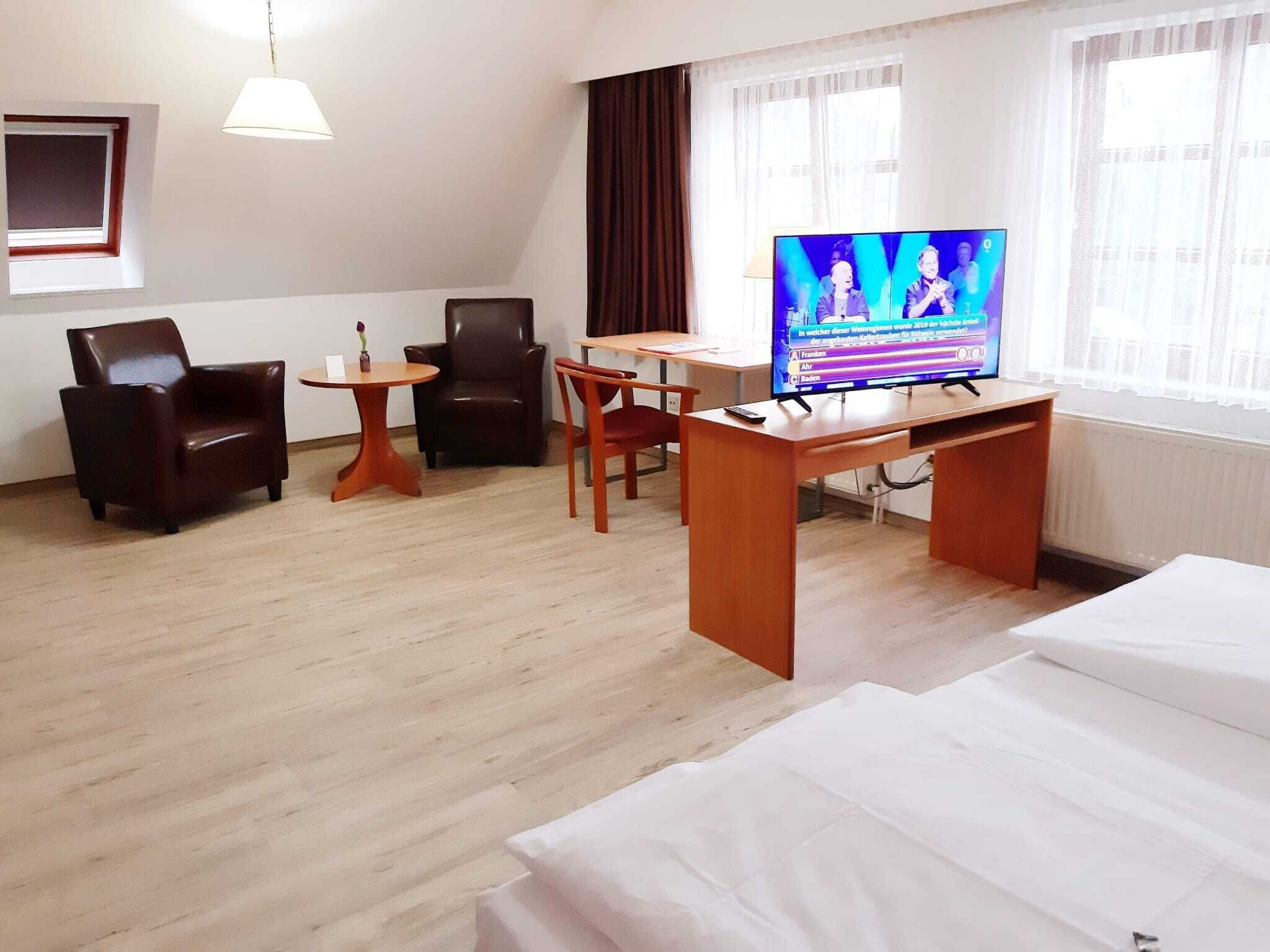 Habitación de hotel con cama, escritorio, dos sillas, una mesita, televisión y ventana.