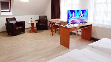Habitación de hotel con cama, escritorio, dos sillas, una mesita, televisión y ventana.