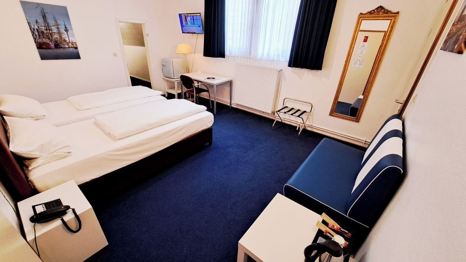 A hotel room with a bed, a desk, a chair, a mirror, and a TV.