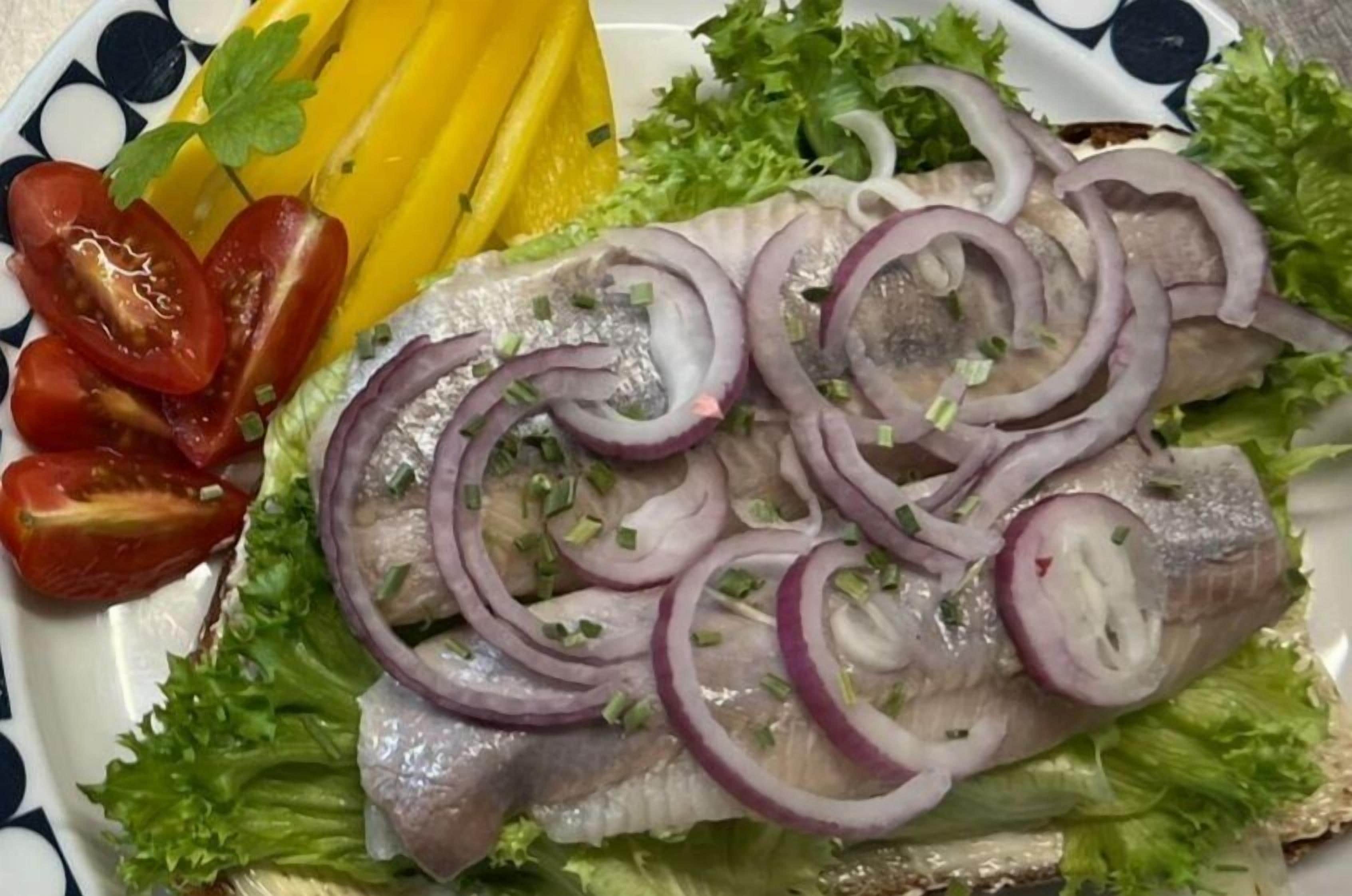 Un plato con un filete de pescado, cebollas rojas en rodajas y tomates cherry sobre una cama de lechuga.