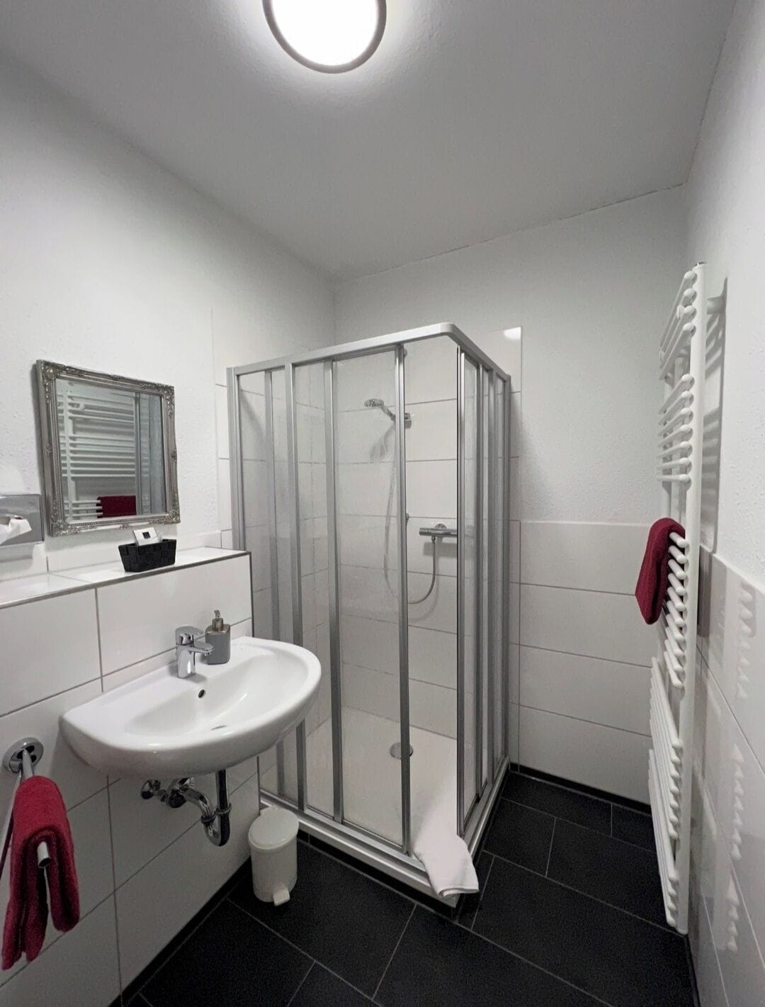 Un baño con cabina de ducha de vidrio, un lavabo blanco, un espejo y un perchero para toallas.