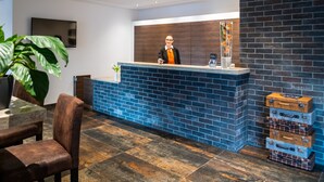 Un área de recepción de diseño moderno, con pared de ladrillo, mostrador de recepción y una planta grande en maceta.