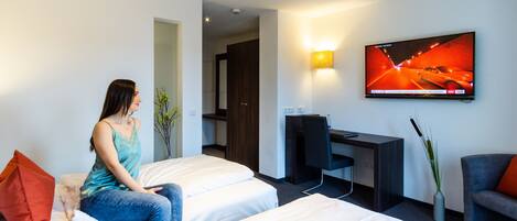 A hotel room with two beds, a desk, a TV, and a chair.