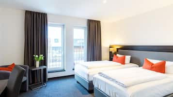 Ein Hotelzimmer mit zwei Betten, einem Schreibtisch und einem Stuhl. Vor den Fenstern hängen Vorhänge und auf dem Schreibtisch steht eine Pflanze.