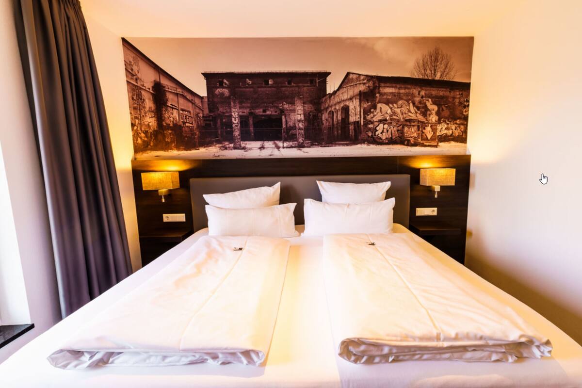 A hotel room with a large bed, two bedside lamps, and a mural on the wall.