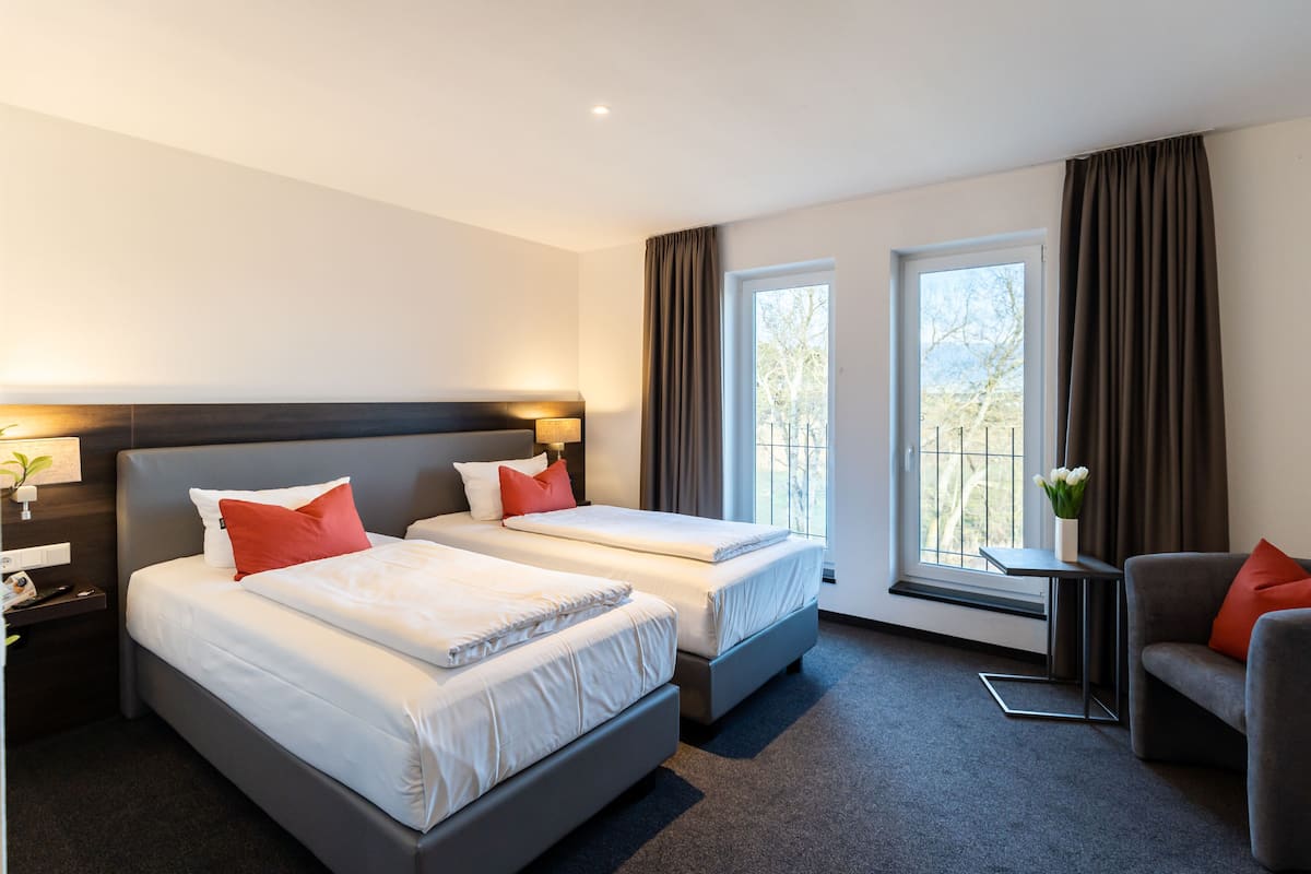 A hotel room with two beds, a sofa, a small table, and a window with curtains.
