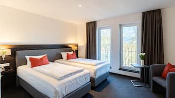 A hotel room with two beds, a sofa, a small table, and a window with curtains.