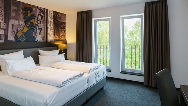 Habitación de hotel con dos camas, un cuadro abstracto grande en la pared, una ventana con cortinas y un escritorio con silla.