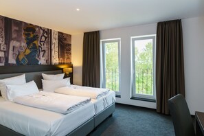 Habitación de hotel con dos camas, un cuadro abstracto grande en la pared, una ventana con cortinas y un escritorio con silla.