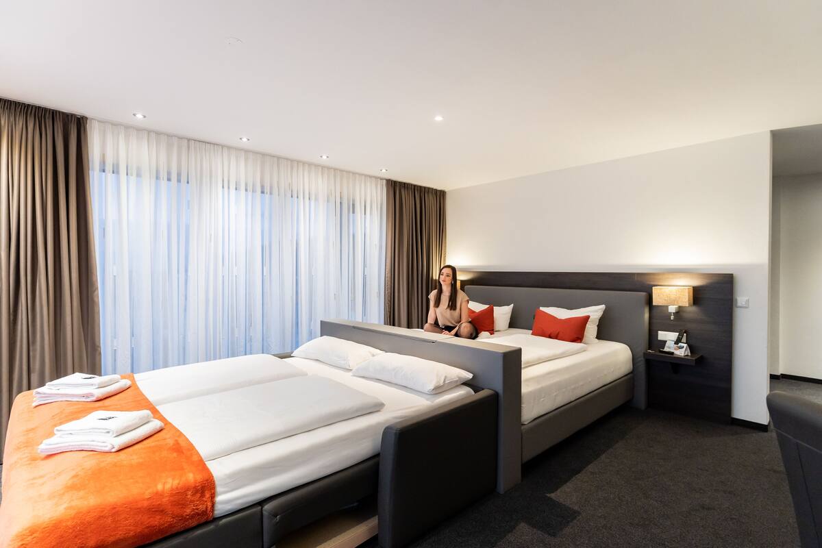 A hotel room with two beds, a nightstand, and a large window with curtains.