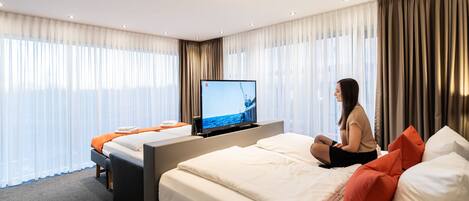 A hotel room with a bed, a television, and a large window with curtains.