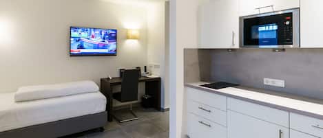A compact hotel room with a bed, a desk, a television, and a kitchenette.