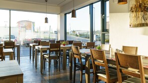Un comedor moderno con mesas y sillas de madera, ventanas amplias e iluminación colgante.