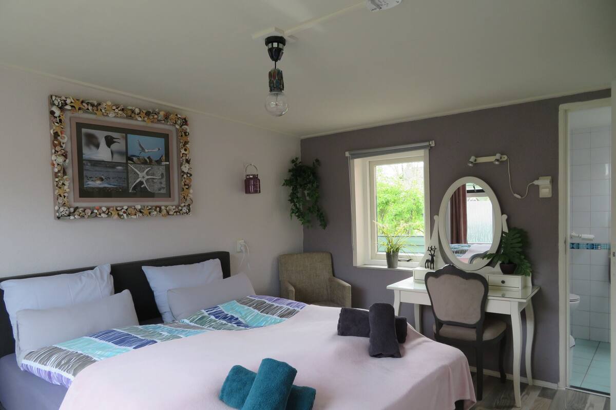 Een slaapkamer met een bed, een bureau, een stoel, een spiegel en een raam.