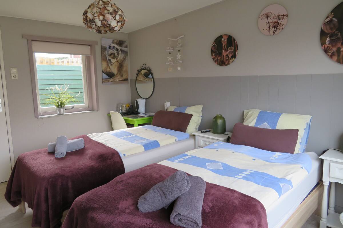 Een hotelkamer met twee bedden, een bureau, een stoel, een raam met uitzicht en wanddecoraties.