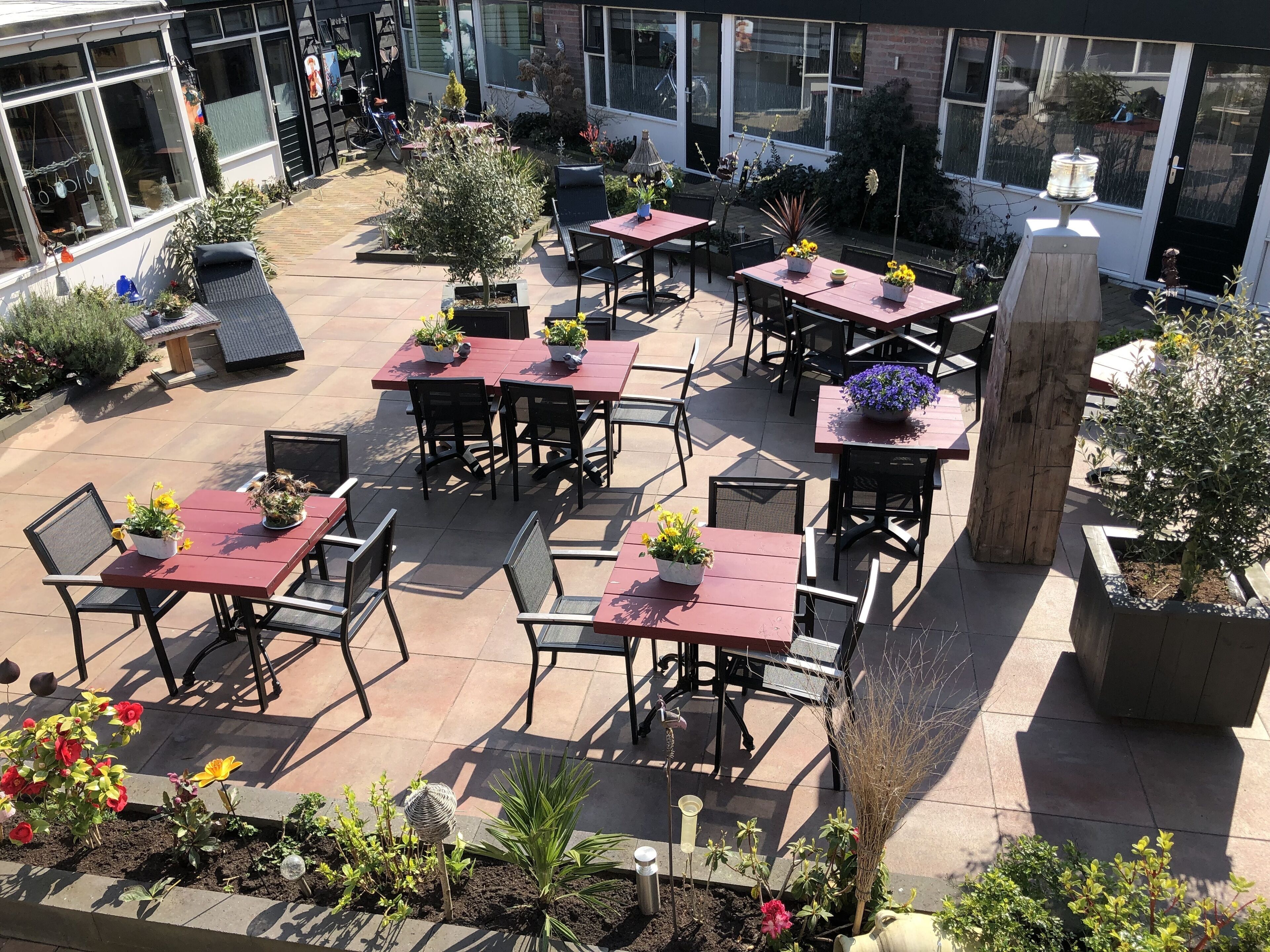 Un patio exterior con varias mesas y sillas, rodeado de plantas y flores en macetas.