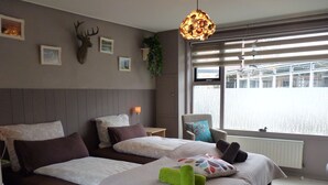 Habitación de hotel con dos camas, un ventanal con persianas, una decoración de cabeza de venado montada en la pared y una lámpara colgante.