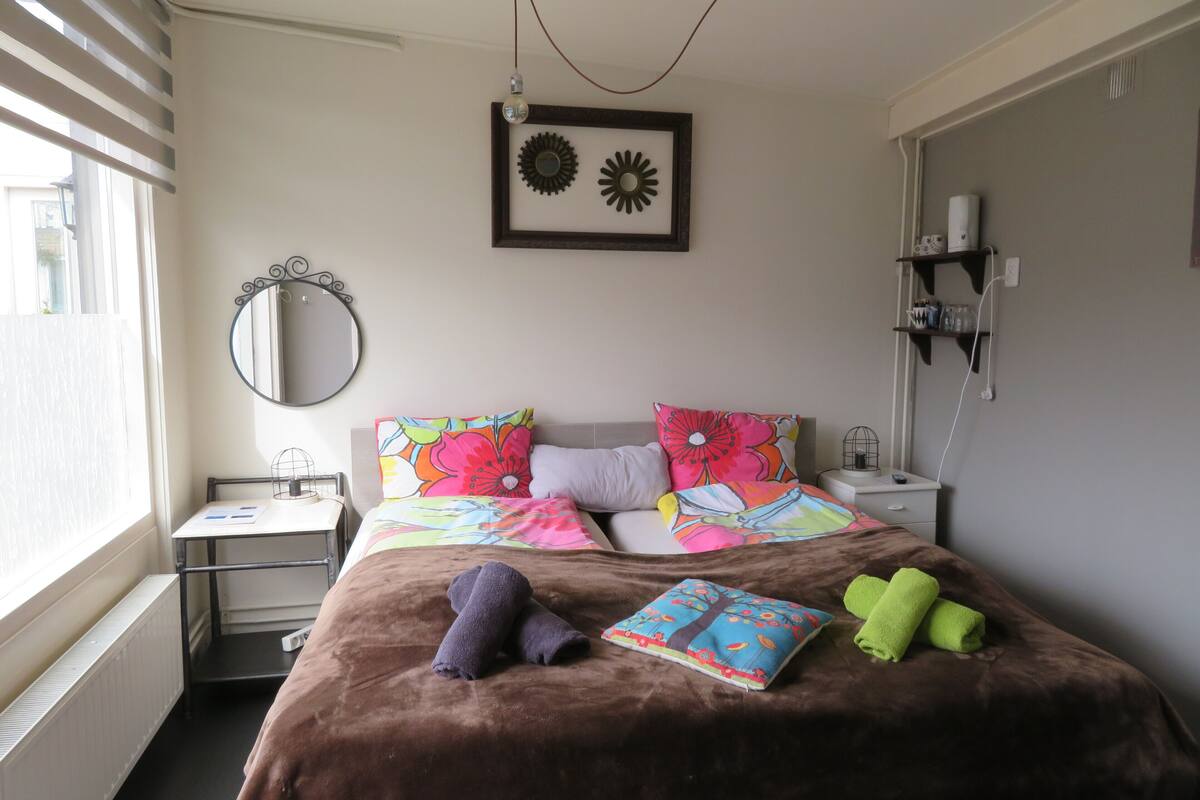 Een slaapkamer met een bed, nachtkastje, spiegel, radiator en een wandplank.