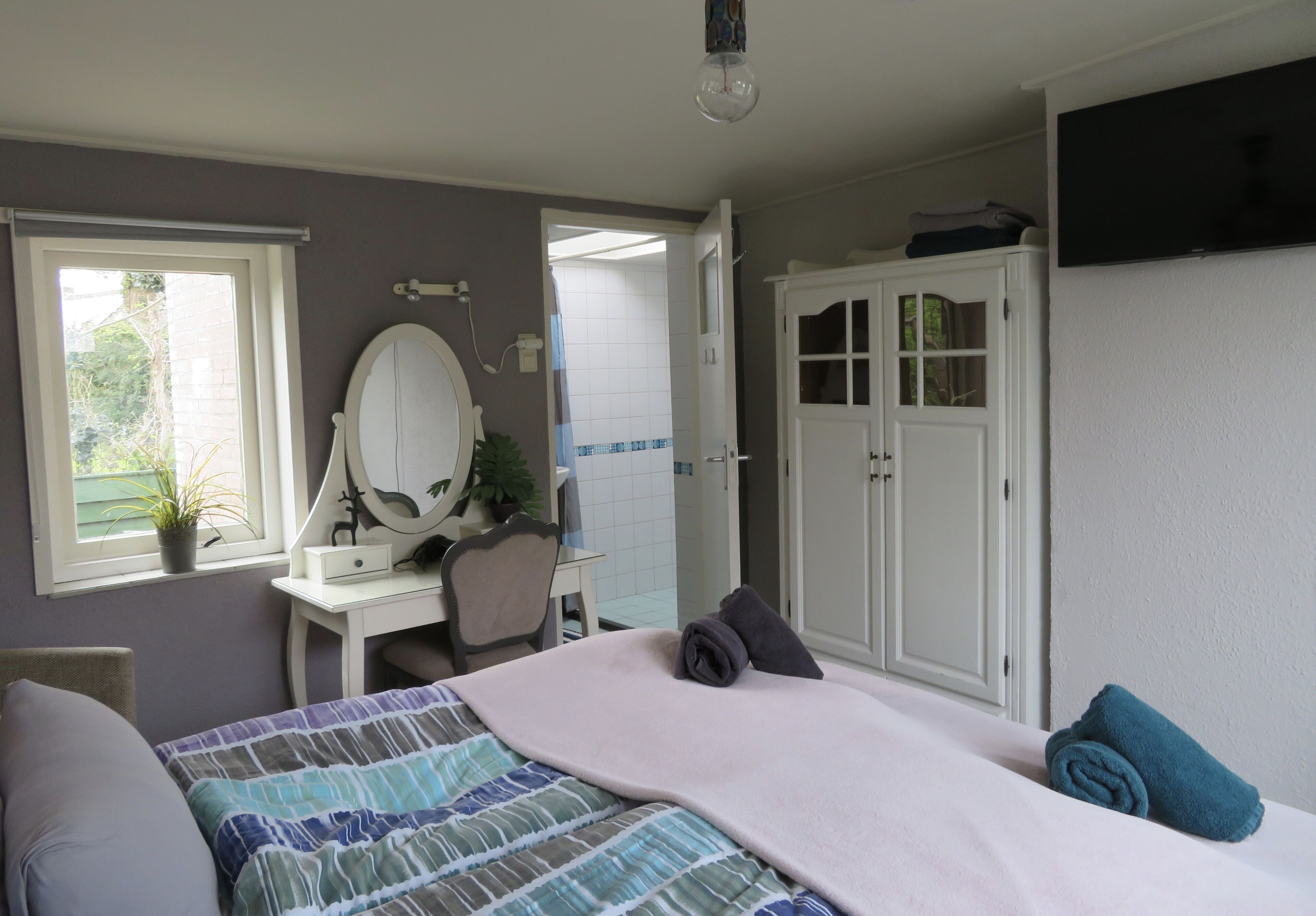 A bedroom with a bed, a desk, a chair, a mirror, and a wardrobe.