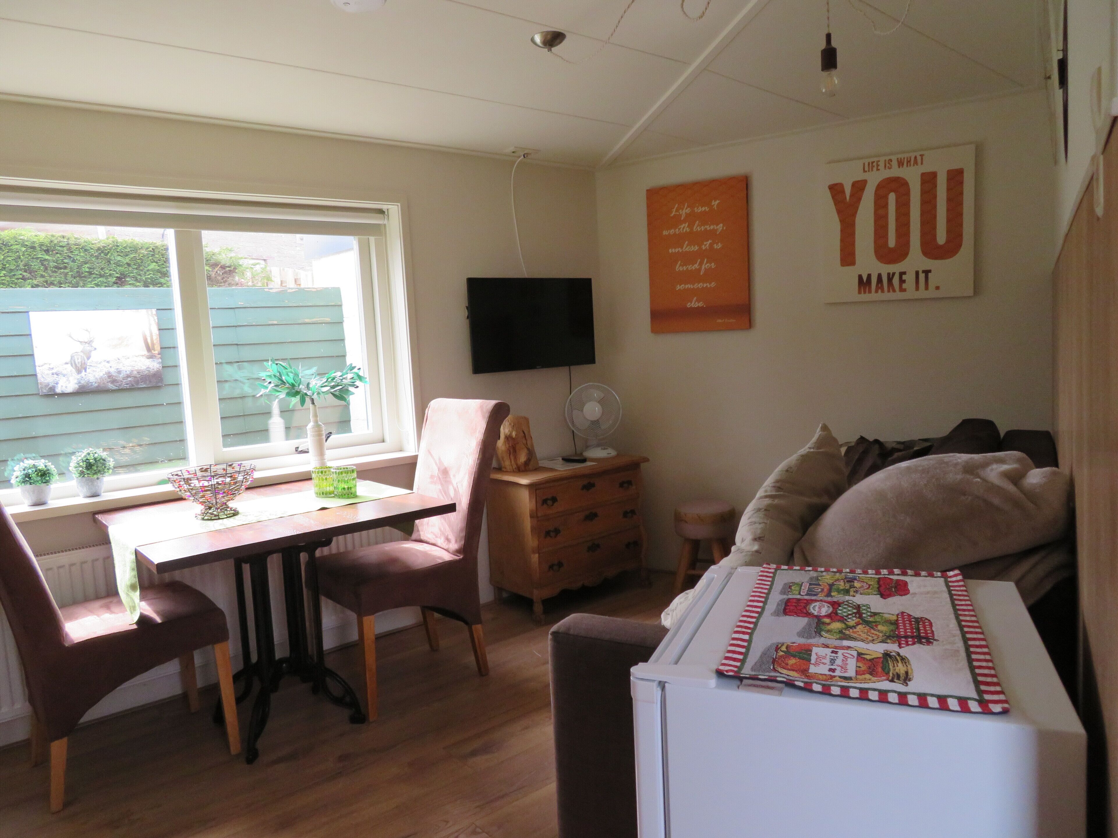A cozy room with a dining table, chairs, a small cabinet, a bed, and a wall-mounted TV.